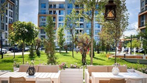 Un espacio al aire libre con mesas y sillas, rodeado de vegetación y vistas a edificios modernos.