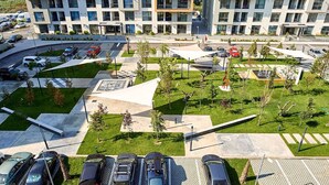 Un estacionamiento con varios coches, rodeado de vegetación y edificios modernos.