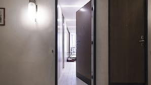 A hallway with a wooden door on the right, a framed picture on the left, and a bright light fixture on the ceiling. - Hemeras Boutique House Aparthotel Duomo 11 (Milan)