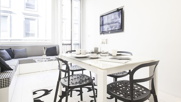 A modern, well-lit living area with a sofa, a dining table with chairs, and a television mounted on the wall. - Hemeras Boutique House Aparthotel Duomo 11 (Milan)