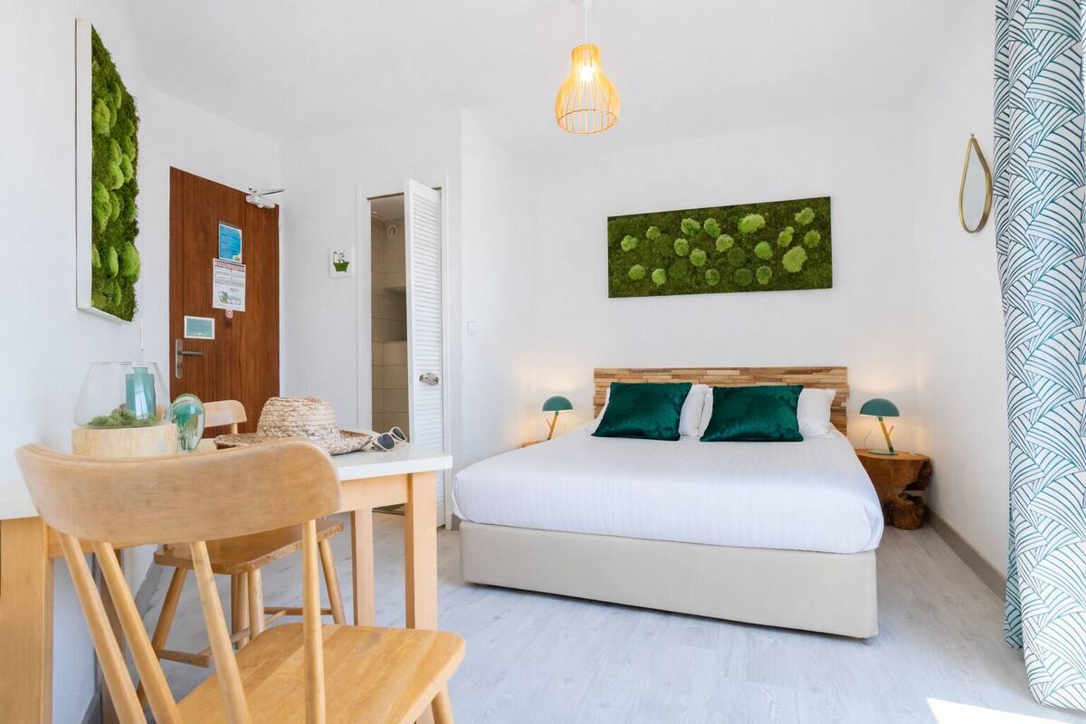 Quarto com cama, escrivaninha, cadeira, luminária pendente e obra de arte na parede.