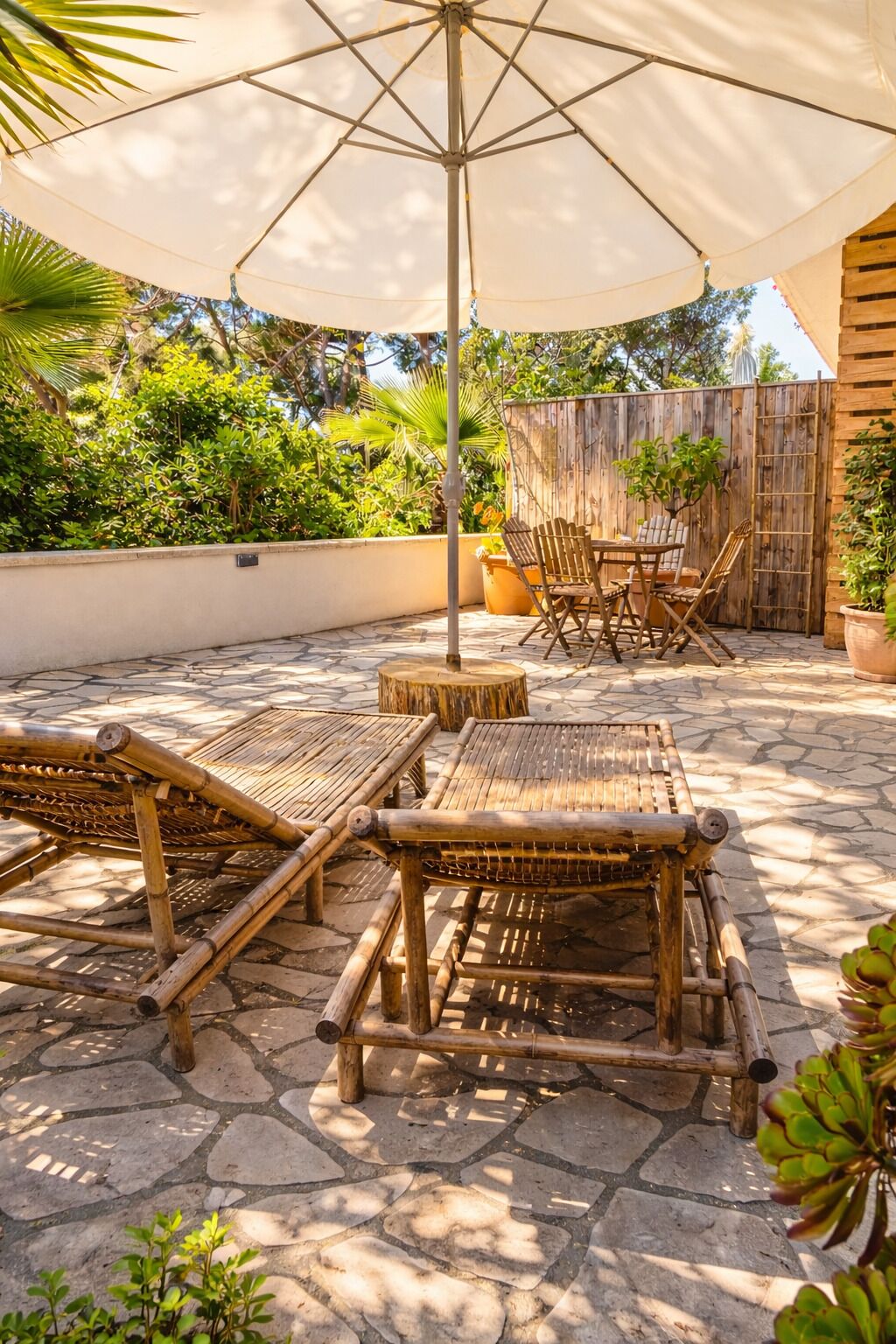 Un patio al aire libre con mobiliario de bambú, un paraguas grande y una valla de madera.