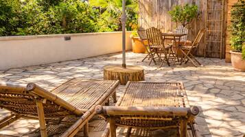 Un patio al aire libre con mobiliario de bambú, un paraguas grande y una valla de madera.