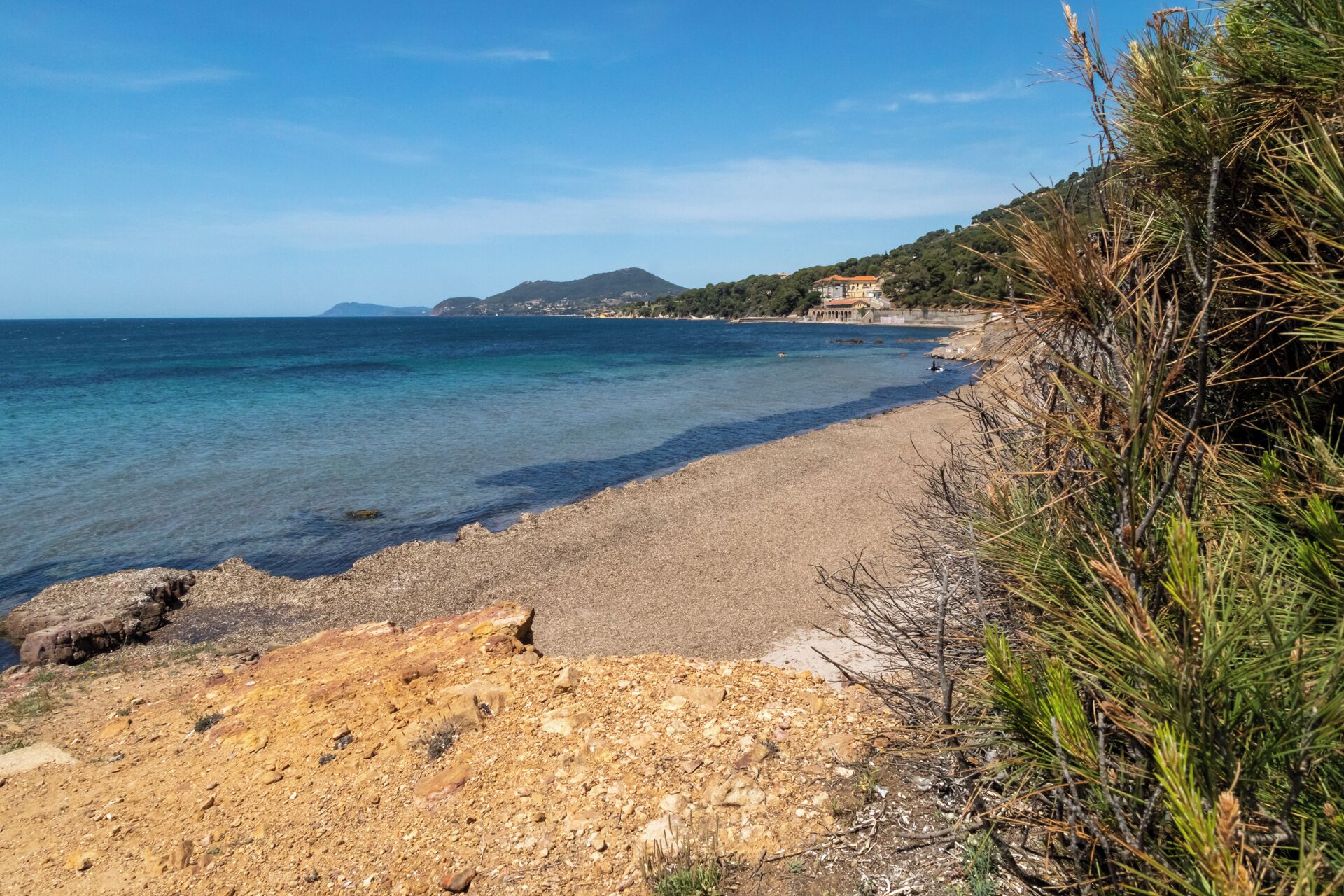 A coastal beach with clear water, rocky terrain, and a distant mountain.