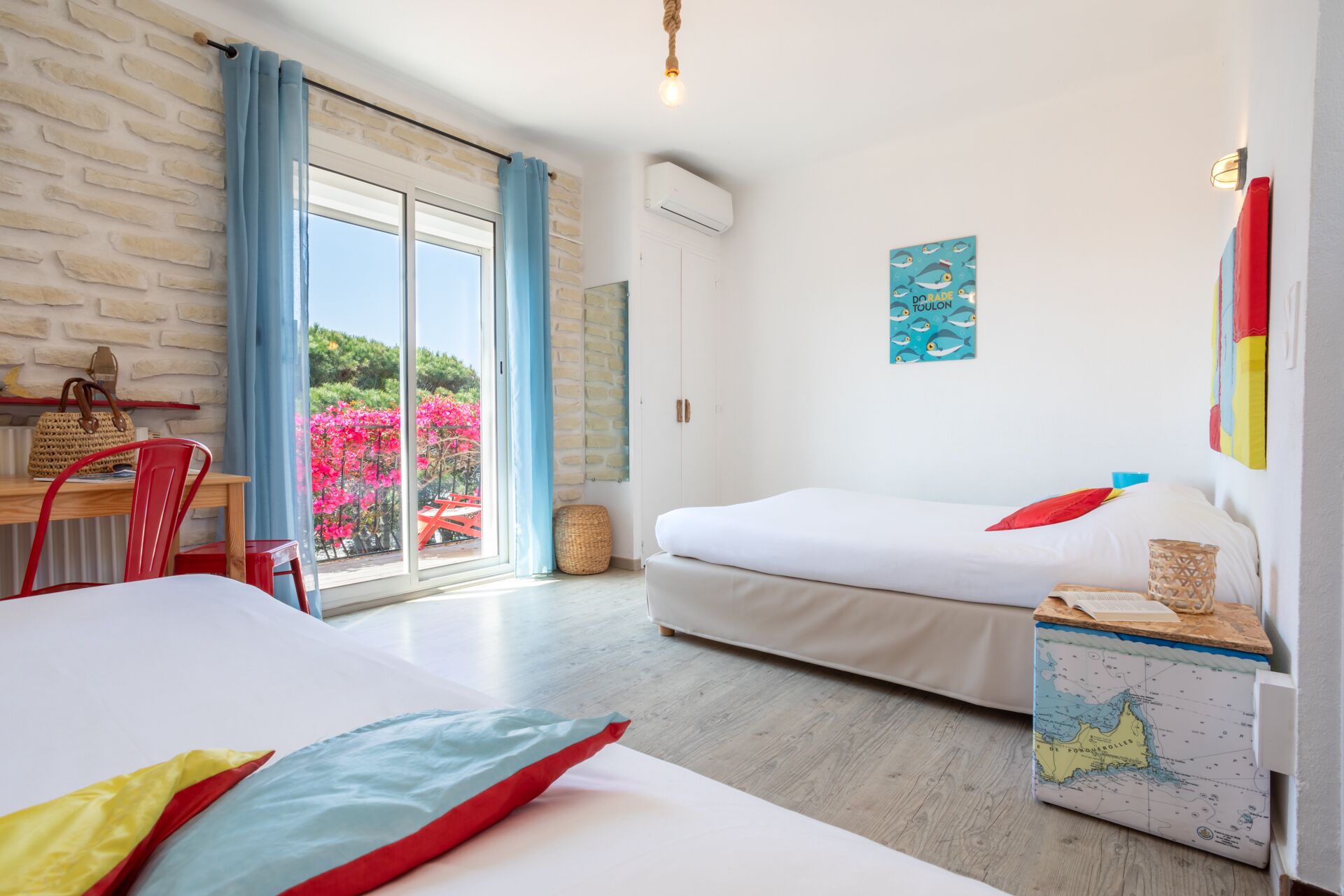 A hotel room with a bed, a desk, and a chair. There is a window with curtains, a map on the nightstand, and a wall with a painting.
