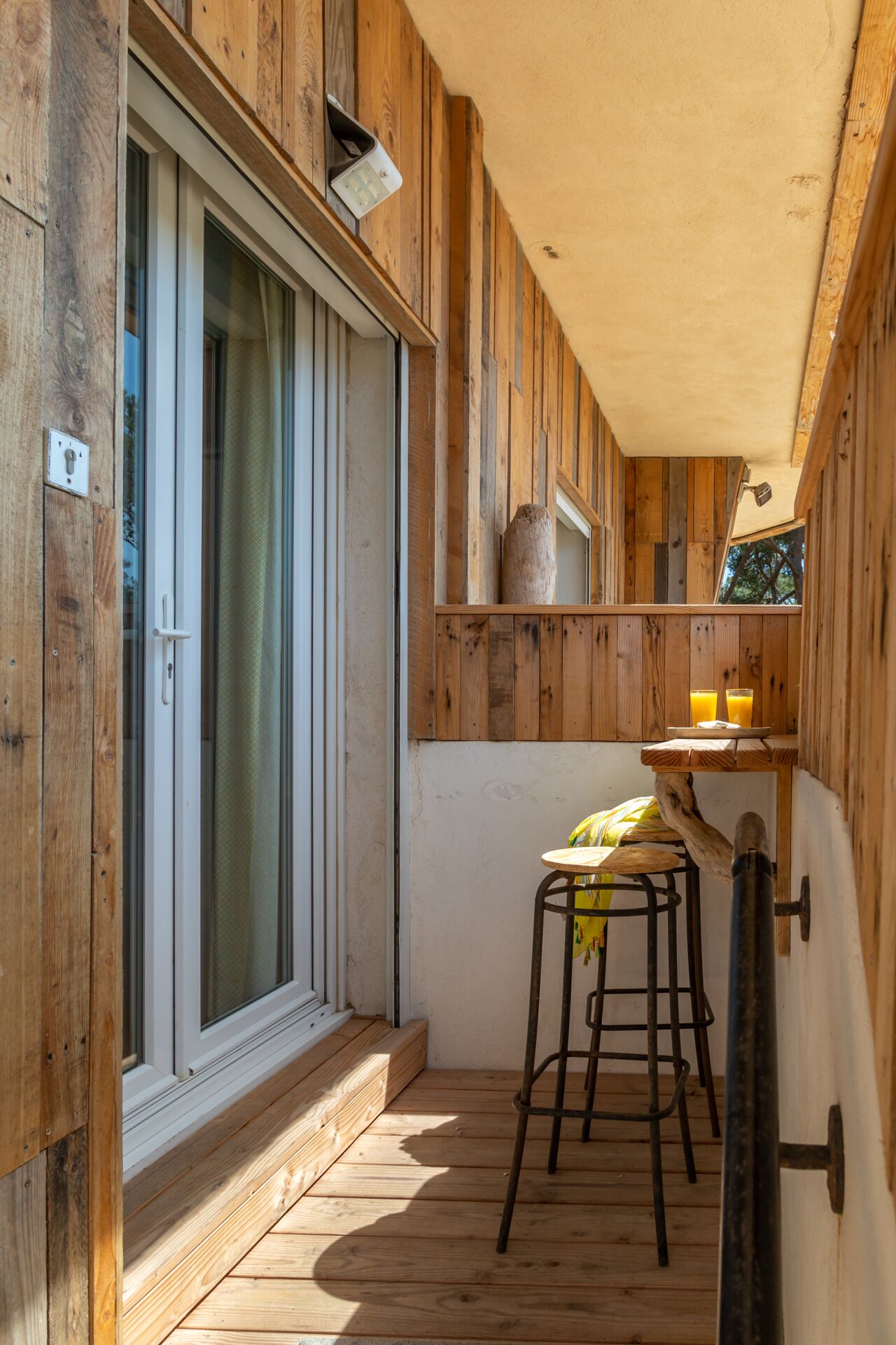 A wooden balcony with a sliding glass door, a small table with stools, and a rustic interior design.