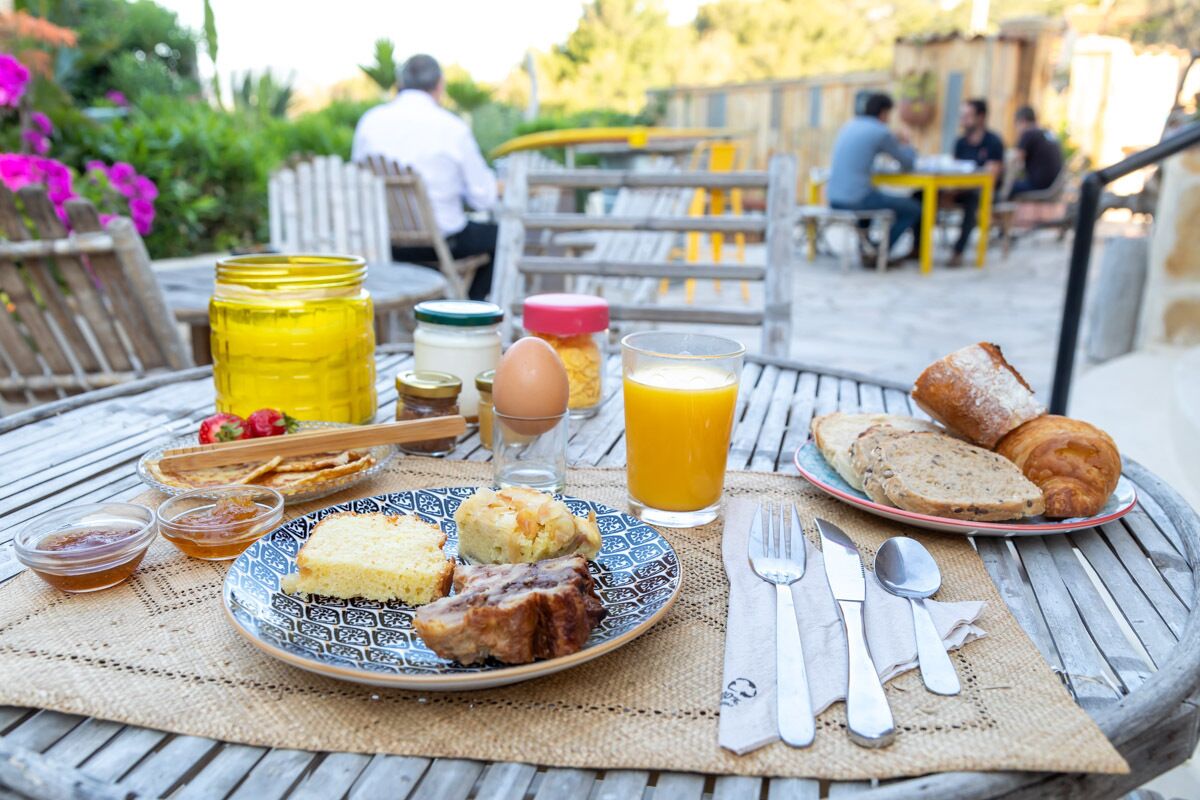 Een ontbijttafel met eten, een glas sinaasappelsap en ontbijtartikelen op een houten tafel buiten.