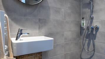 A modern bathroom with a white sink, a round mirror, and a shower.