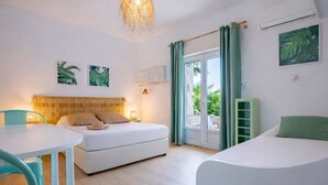 Una habitación con cama, una mesita, una silla, una lámpara colgante y vistas a través de un ventanal.