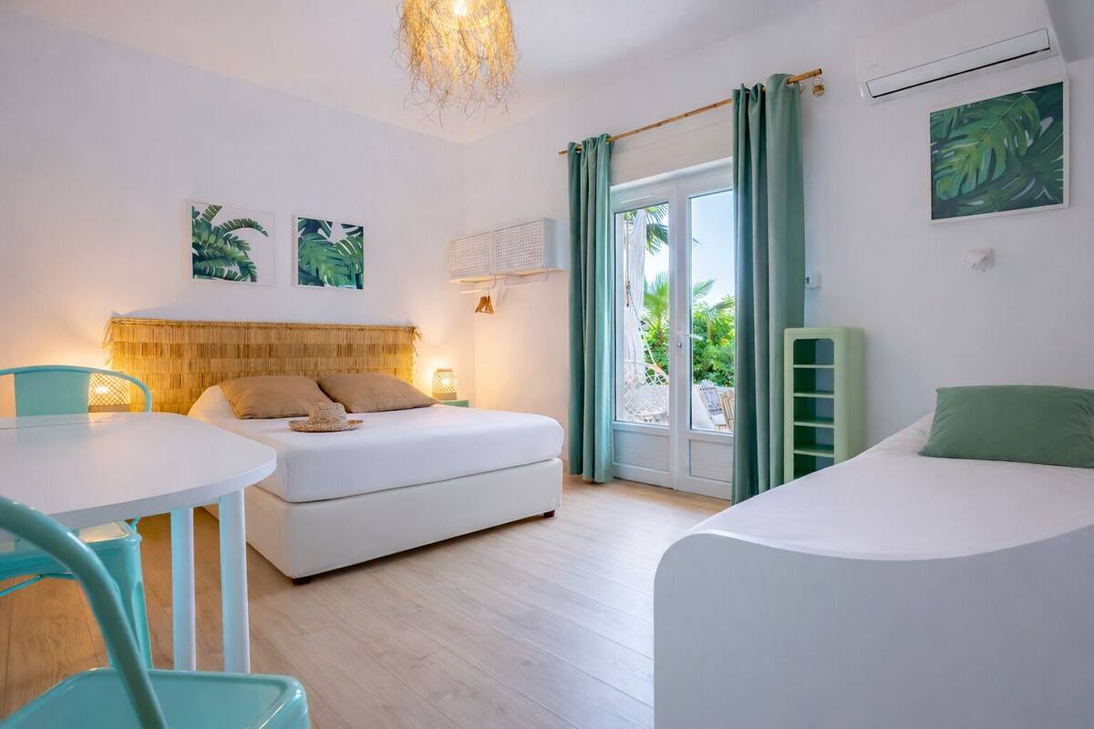 Quarto com cama, uma pequena mesa, uma cadeira, luminária pendente e vista através de uma porta de vidro.