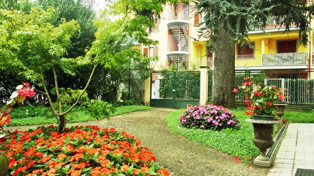 A garden with red flowers, a pathway, and a building with balconies. - Villa Laila (Lodi)