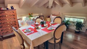 A dining area with a wooden table set for four, surrounded by chairs. A decorative wooden cabinet is to the left, and a potted plant is in the foreground. - Villa Laila (Lodi)