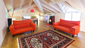 A spacious loft with high ceilings and exposed beams, featuring two vibrant orange sofas and a patterned rug on a wooden floor. - Villa Laila (Lodi)
