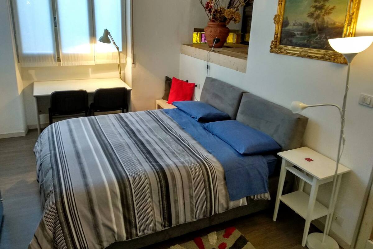 Ein Schlafzimmer mit einem Bett, einem Schreibtisch, einem Stuhl, einer Lampe und einem Bild an der Wand.