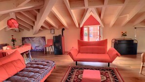 A spacious loft with exposed wooden beams, a dining area with a red table and chairs, a large window, and a cozy seating area with a patterned rug. - Villa Laila (Lodi)