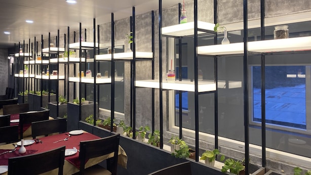 A modern dining area with multiple tables, black chairs, and white shelves with plants. - Hotel Aarunya Royale (Luni)