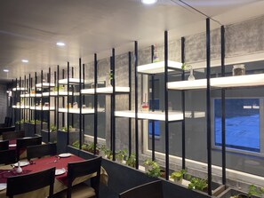 Un comedor moderno con varias mesas, sillas negras y estantes blancos con plantas.