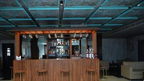A bar area with wooden counter and stools, a ceiling with a blue pattern, and a tiled floor. - Hotel Aarunya Royale (Luni)