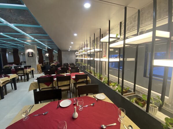Un restaurante moderno con techos altos, vigas a la vista y una hilera de mesas con manteles rojos.