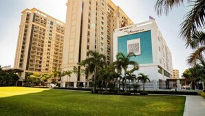 A high-rise hotel with multiple floors, a prominent blue and white facade, and a well-maintained lawn in the foreground. - Hotel Aarunya Royale (Luni)