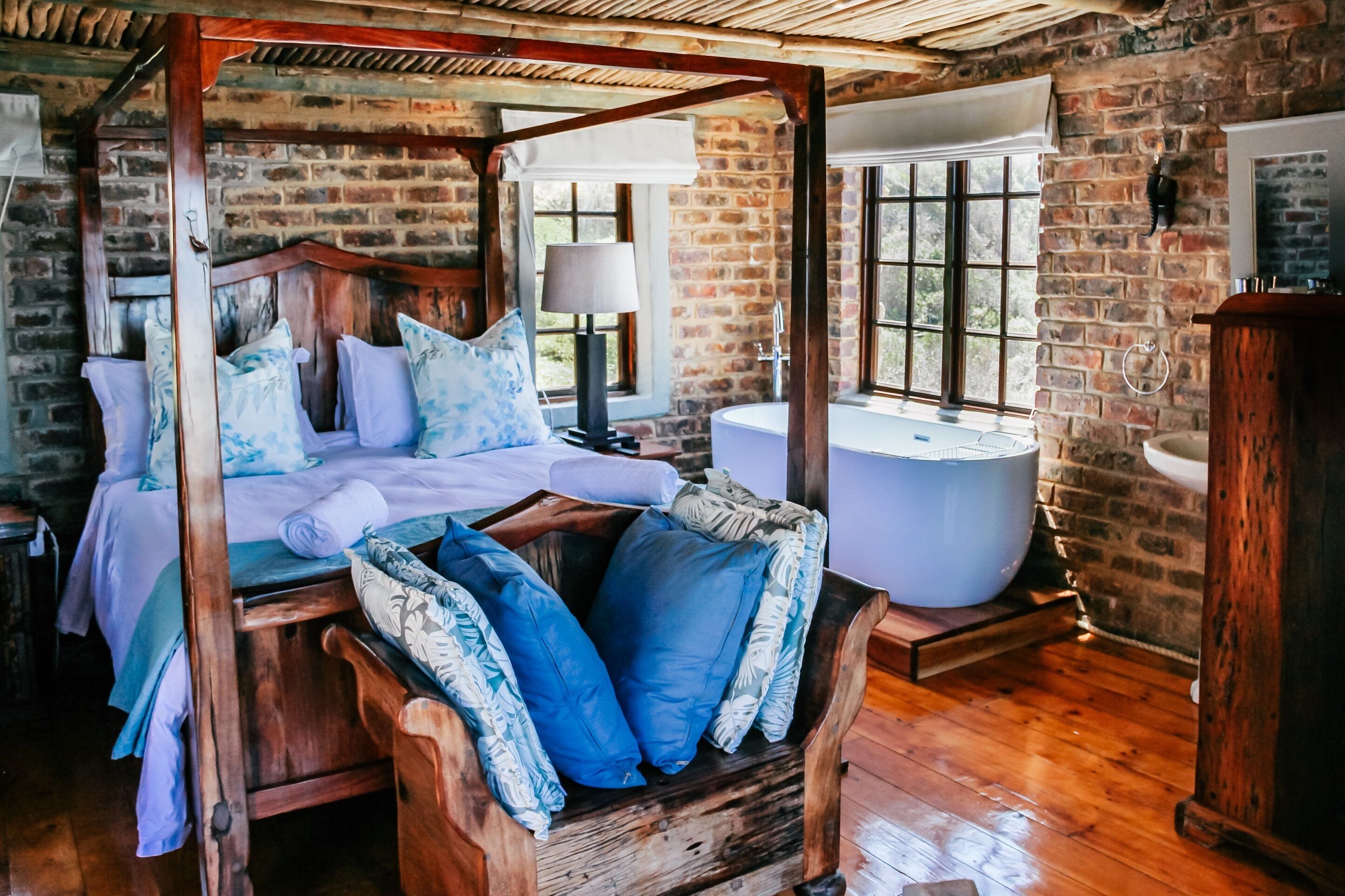 A four-poster bed with a wooden canopy, a large bathtub, and a rustic brick wall.
