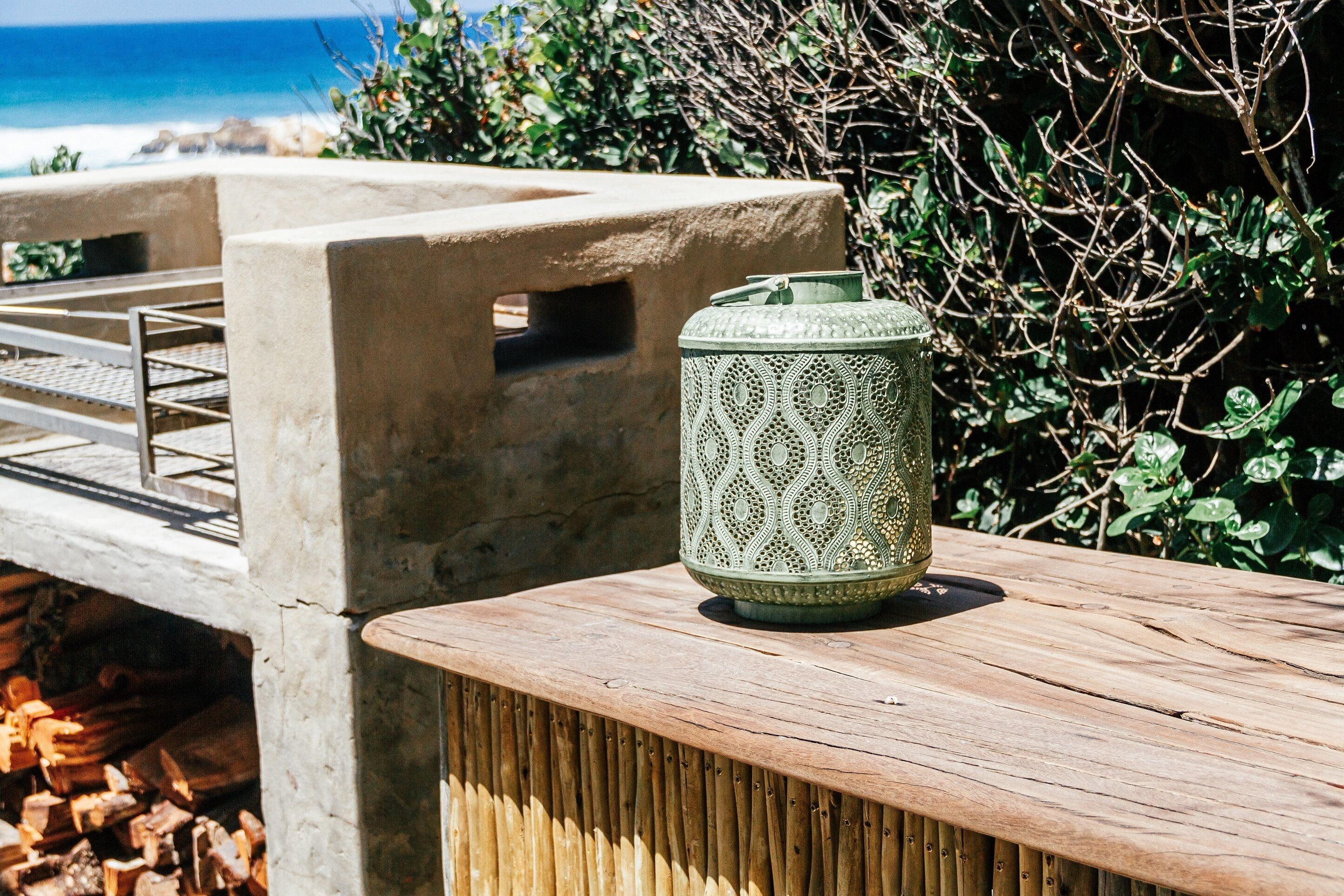 A concrete bench with a metal railing, a green patterned lantern, and a wooden table.