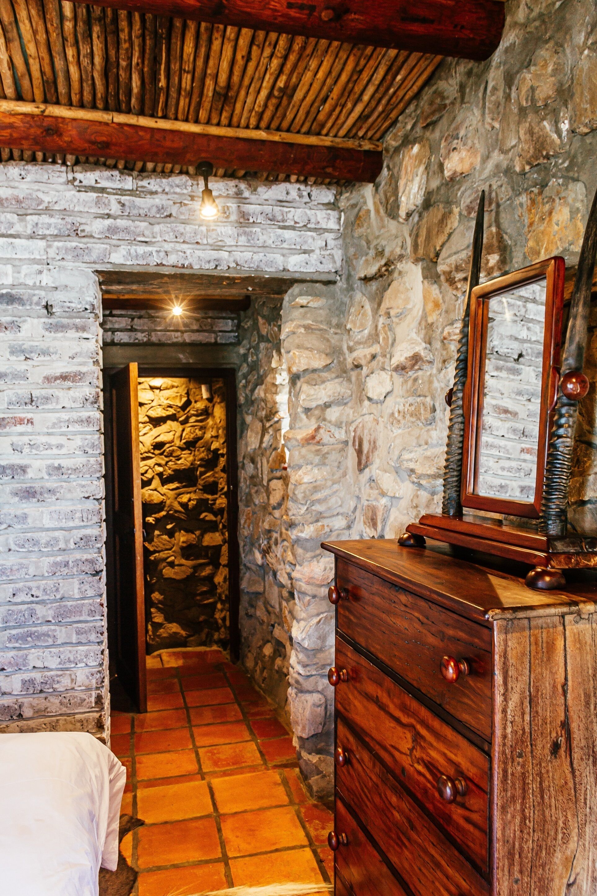 A rustic room with a stone wall, wooden ceiling, and a wooden dresser with drawers.