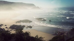 A coastal landscape with a beach, rocky outcrops, and a mountain in the background. - Buccara Noetzie - Lindsay Castle (Knysna)