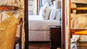 A stone-walled room with a bed, a wooden chair, and a ladder. - Buccara Noetzie - Lindsay Castle (Knysna)
