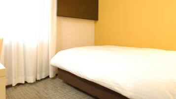 A hotel room with a bed, a flat-screen TV mounted on the wall, and a window with curtains.