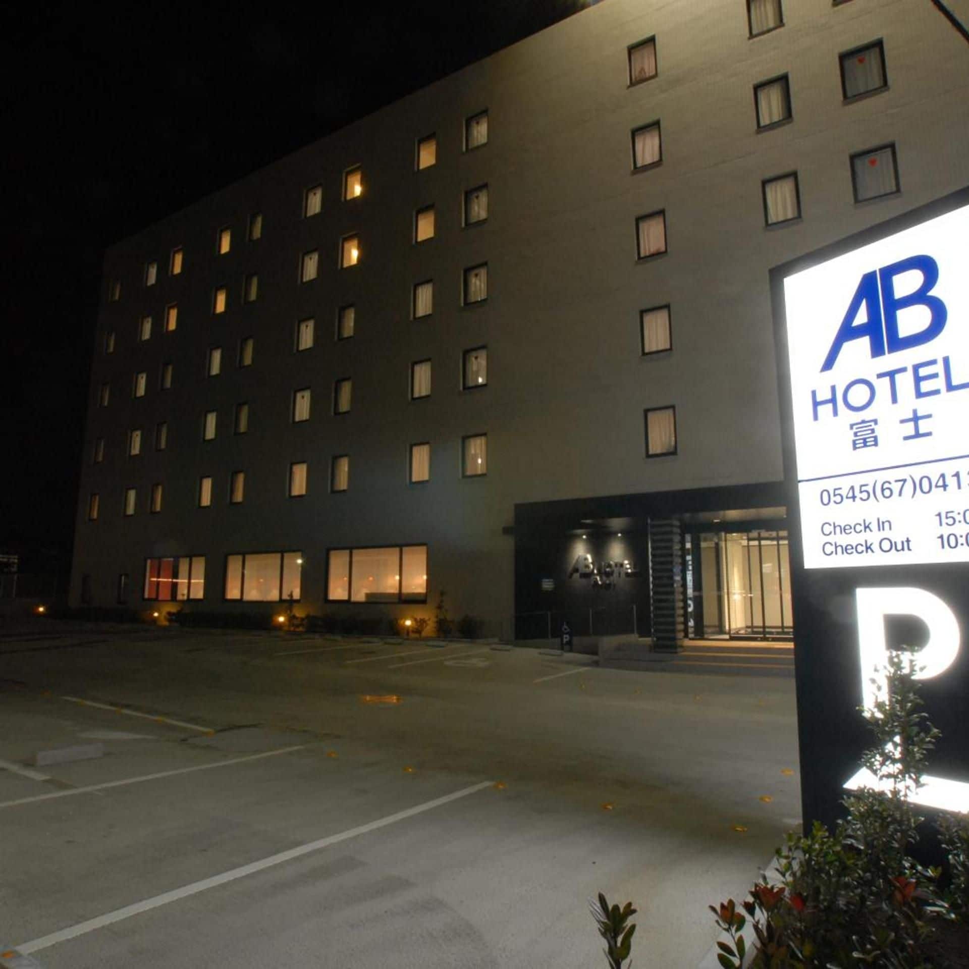 A hotel building with multiple windows, a parking lot, and a signboard with check-in and check-out times.