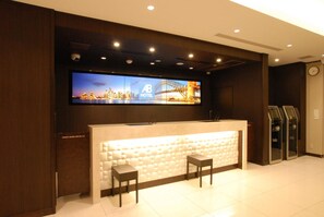 A hotel reception area with a large digital screen, a reception desk, two chairs, and a clock on the wall. - Ab Hotel Fuji (Fuji)