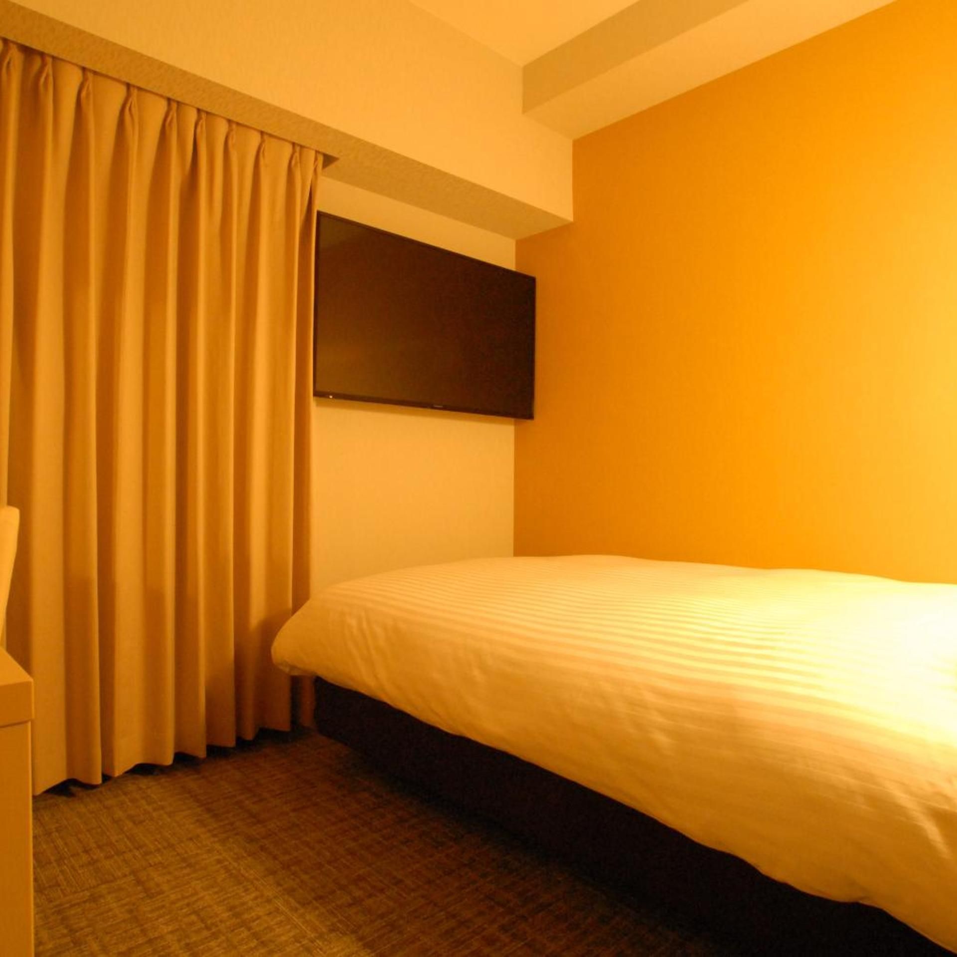 A hotel room with a bed, a flat-screen TV mounted on the wall, and a curtain.