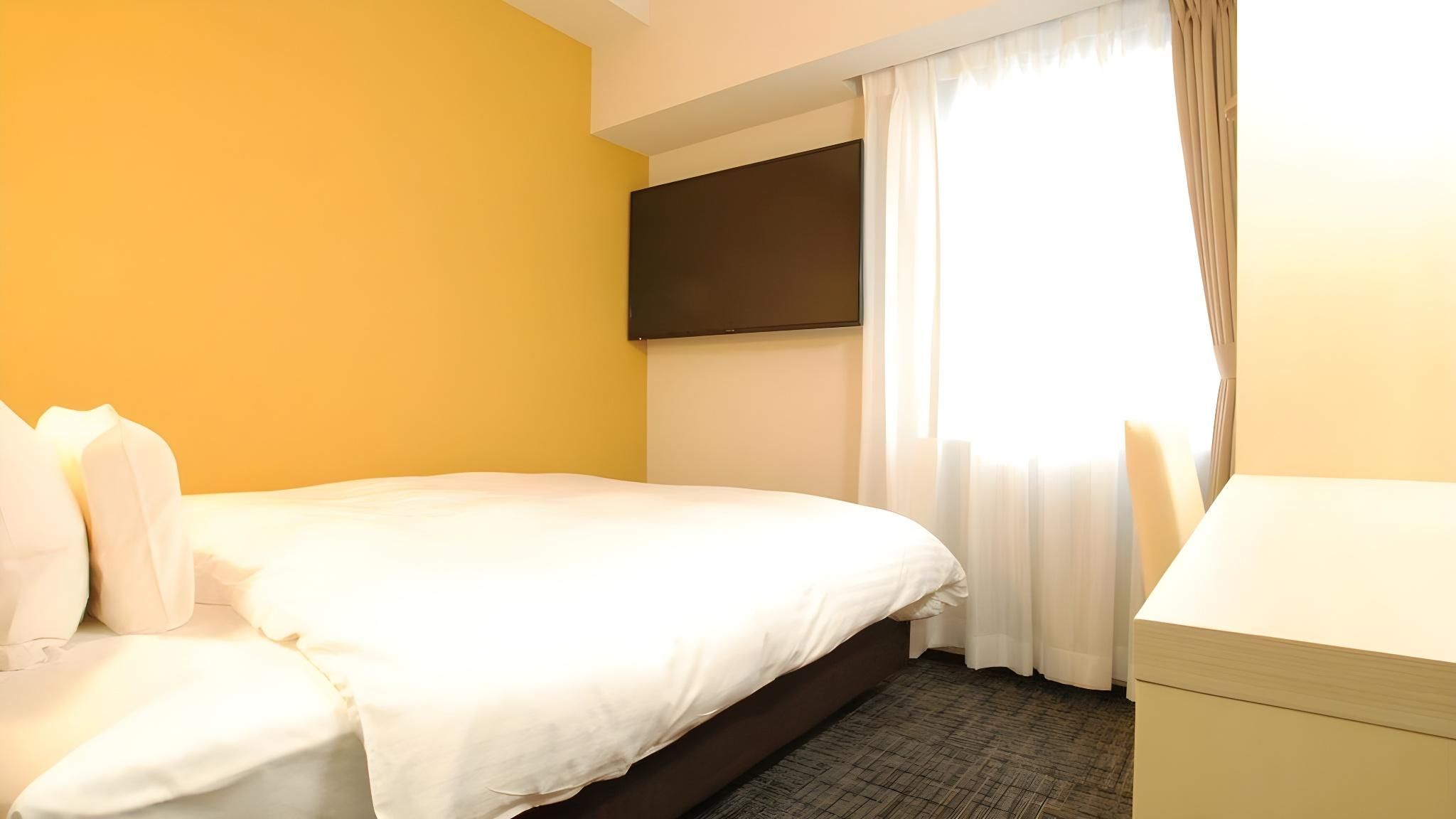Een hotelkamer met een bed, een flatscreen televisie aan de muur en een bureau met een stoel.