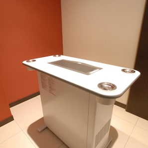 Un objeto blanco y rectangular con una abertura en la parte superior, posiblemente un calentador o purificador de aire, frente a una pared con piso de baldosas.