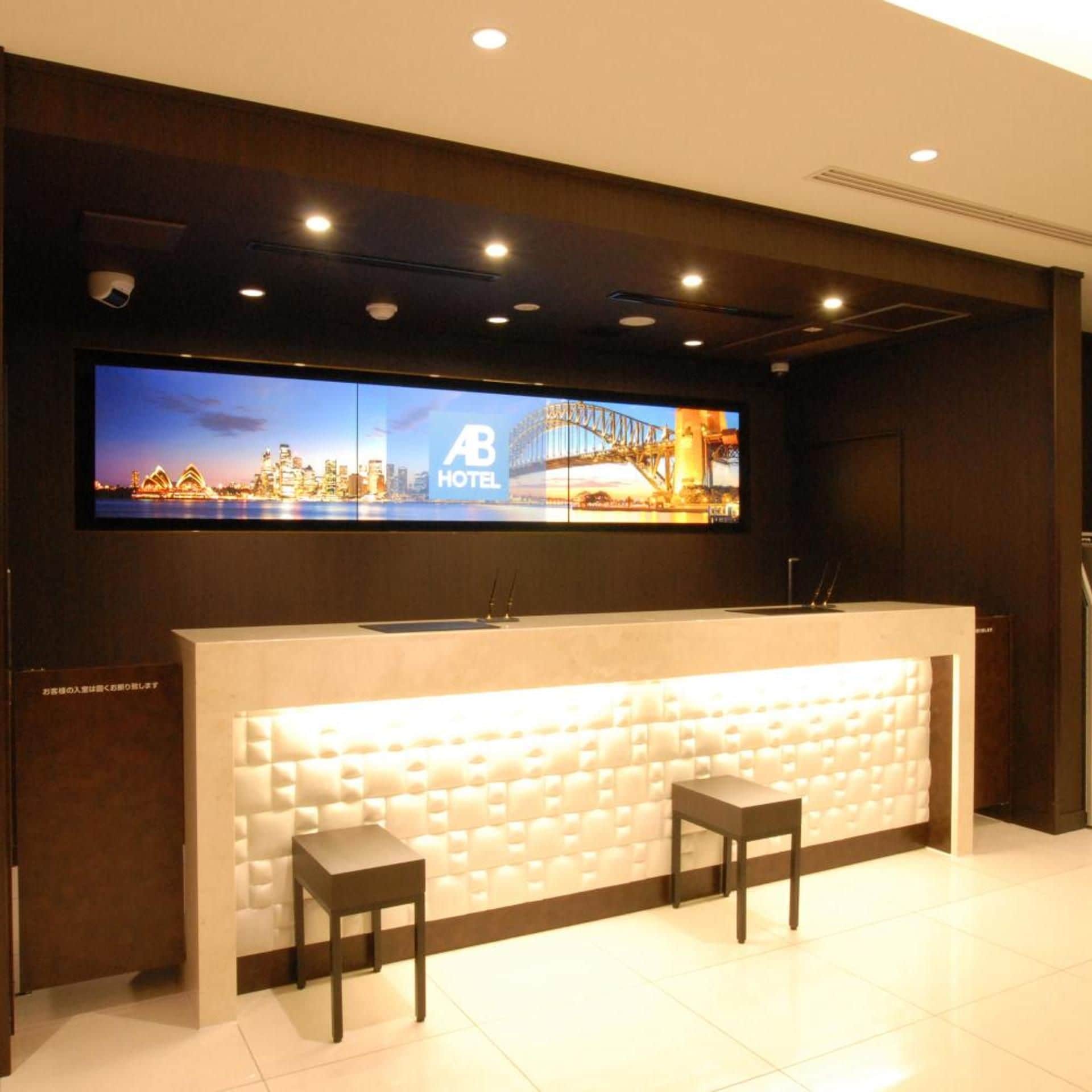 A hotel reception desk with a large digital display above it, two chairs, and a modern design.