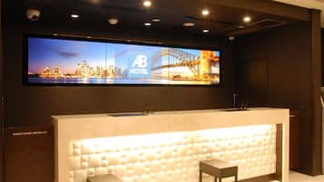 A hotel reception desk with a large digital display above it, two chairs, and a modern design.