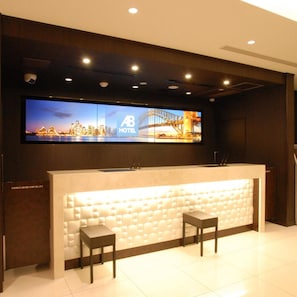 Balcão de recepção de hotel com um grande display digital acima, duas cadeiras e design moderno.
