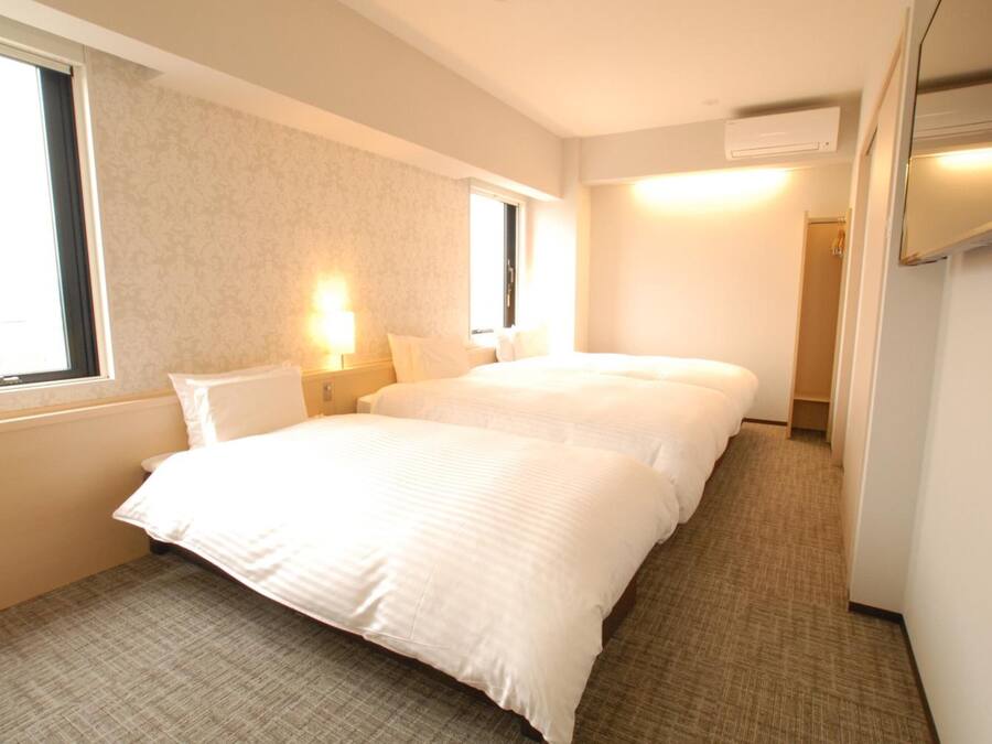 Habitación de hotel con dos camas, una ventana, aire acondicionado de pared y suelo alfombrado.
