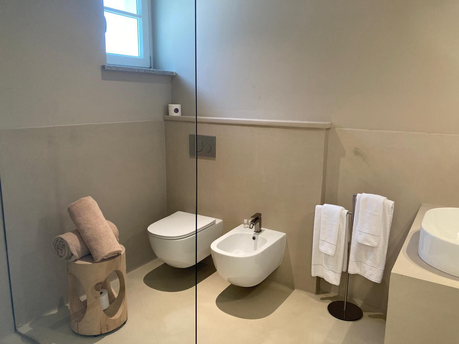 Un baño moderno con inodoro, bidé y bañera. Hay un perchero con toallas y un sujetatelas de madera con una toalla enrollada.