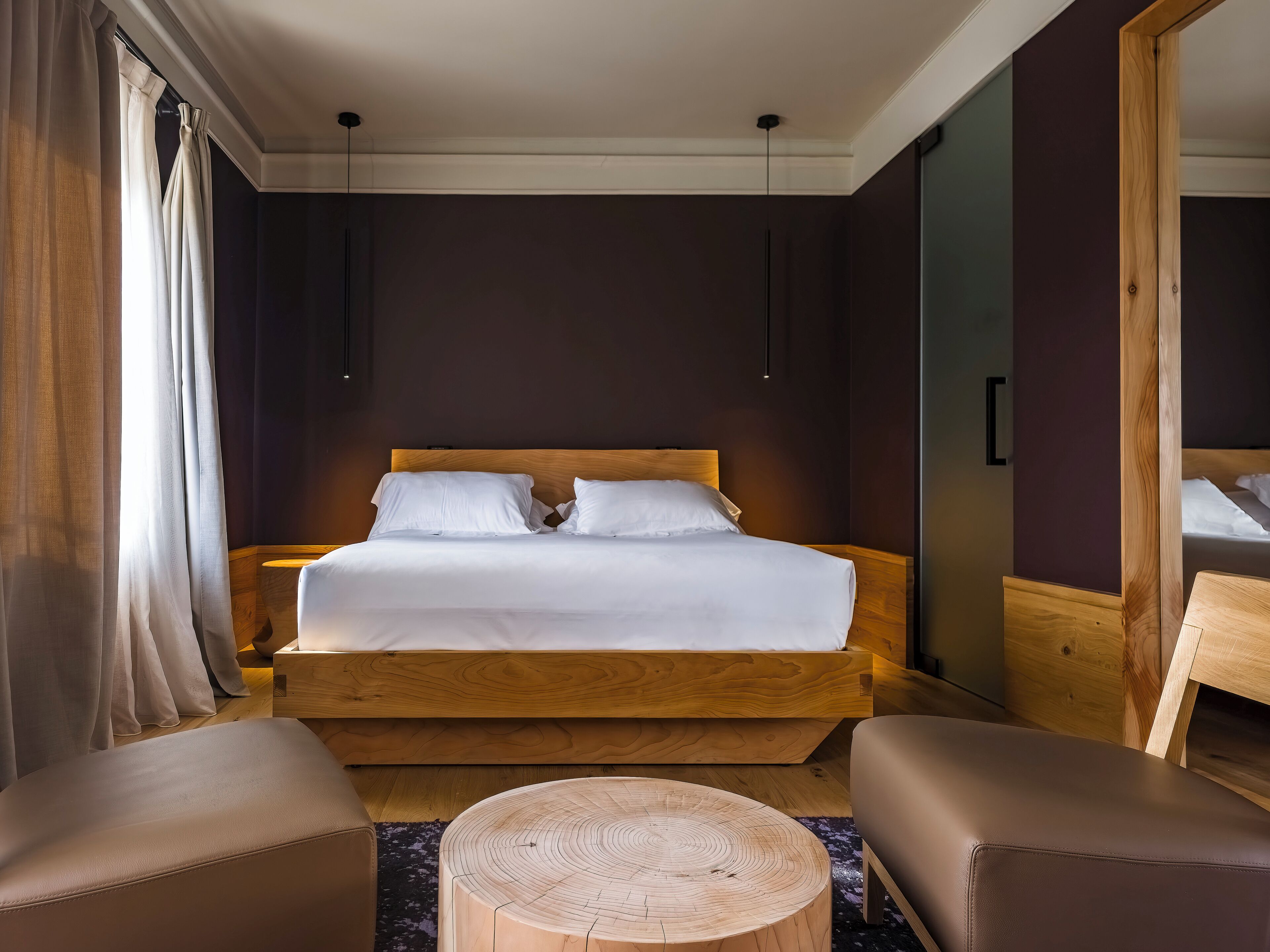 A modern hotel room with a large bed, wooden headboard, and a round wooden table.