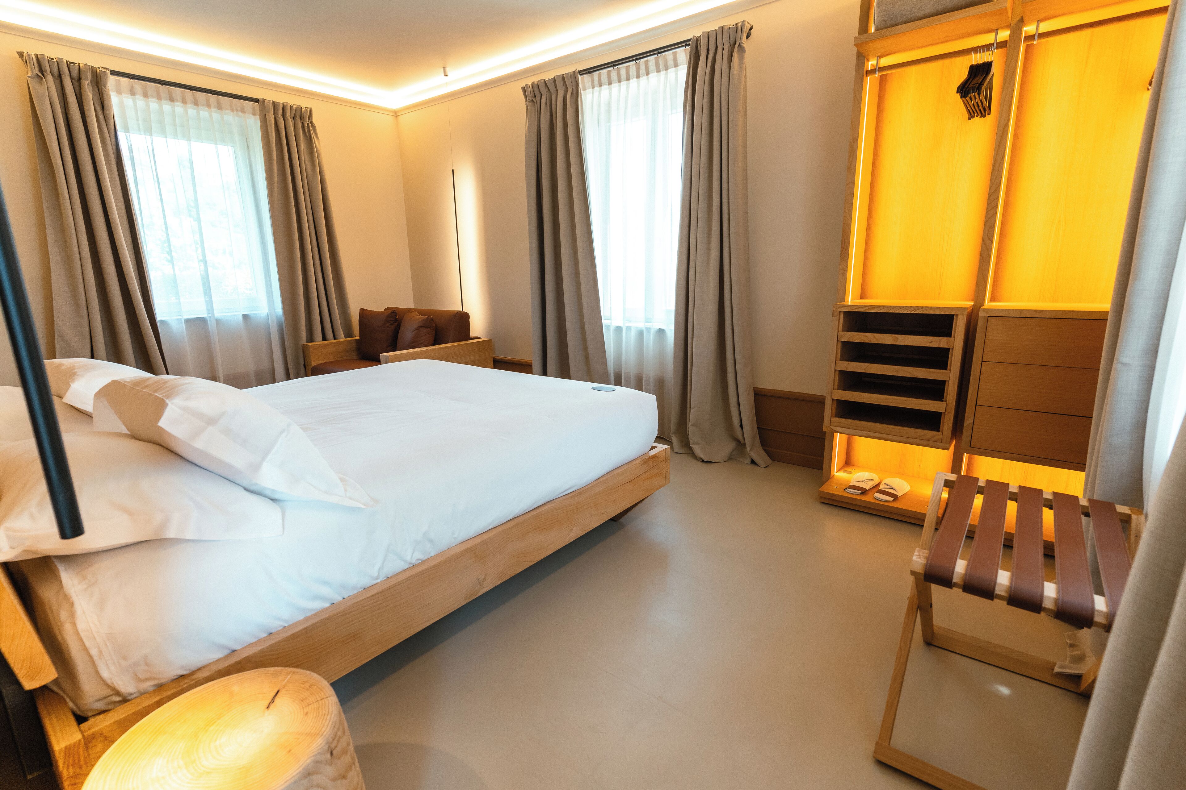 Ett modernt hotellrum med en stor säng, ett träbeklätt sänggavel och en inbyggd bänk med förvaringsutrymme.