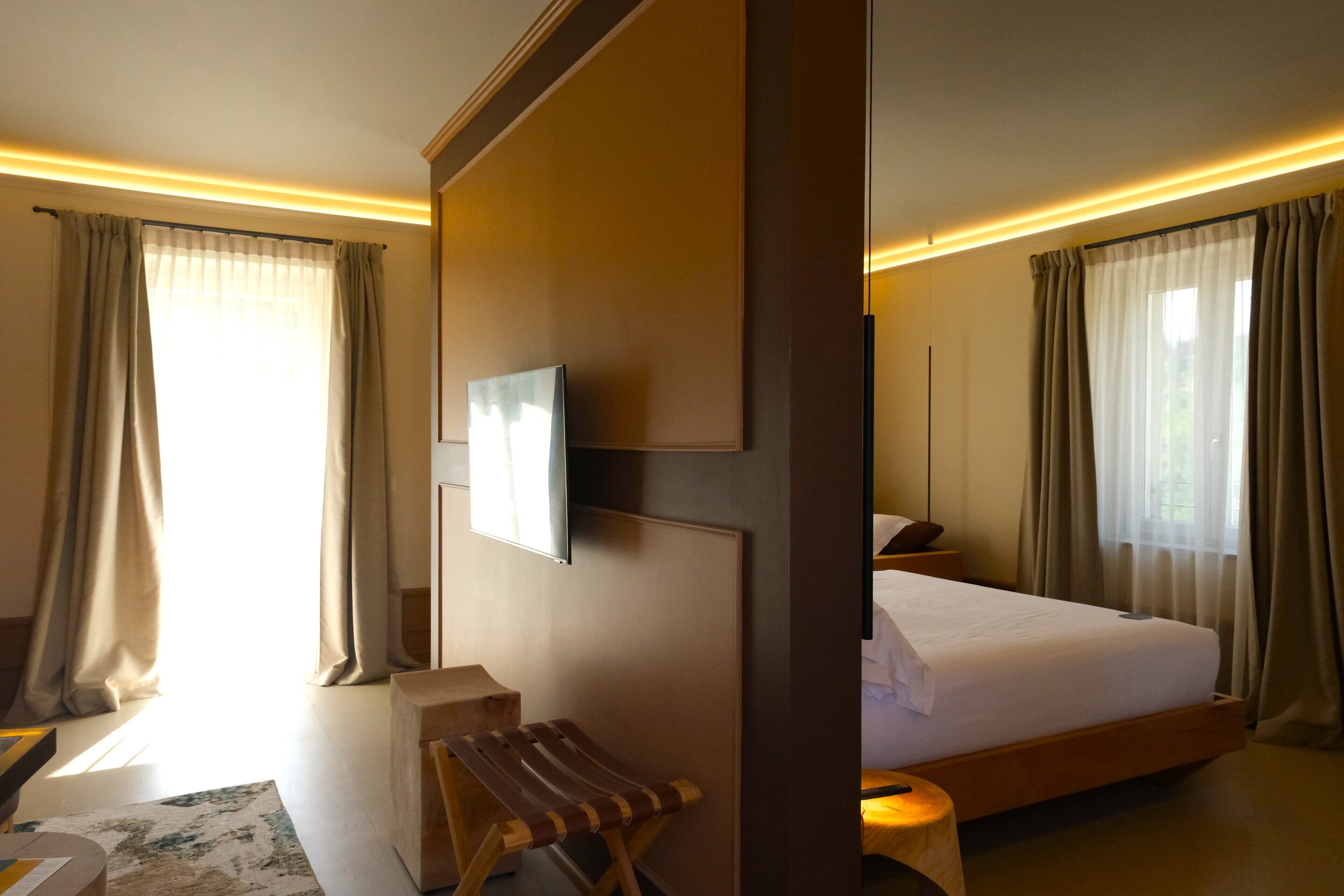 A hotel room with a bed, a desk, a chair, and a large window with curtains.