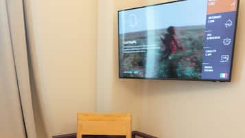 A room with a wooden chair, a round wooden table, and a wall-mounted TV displaying a menu.