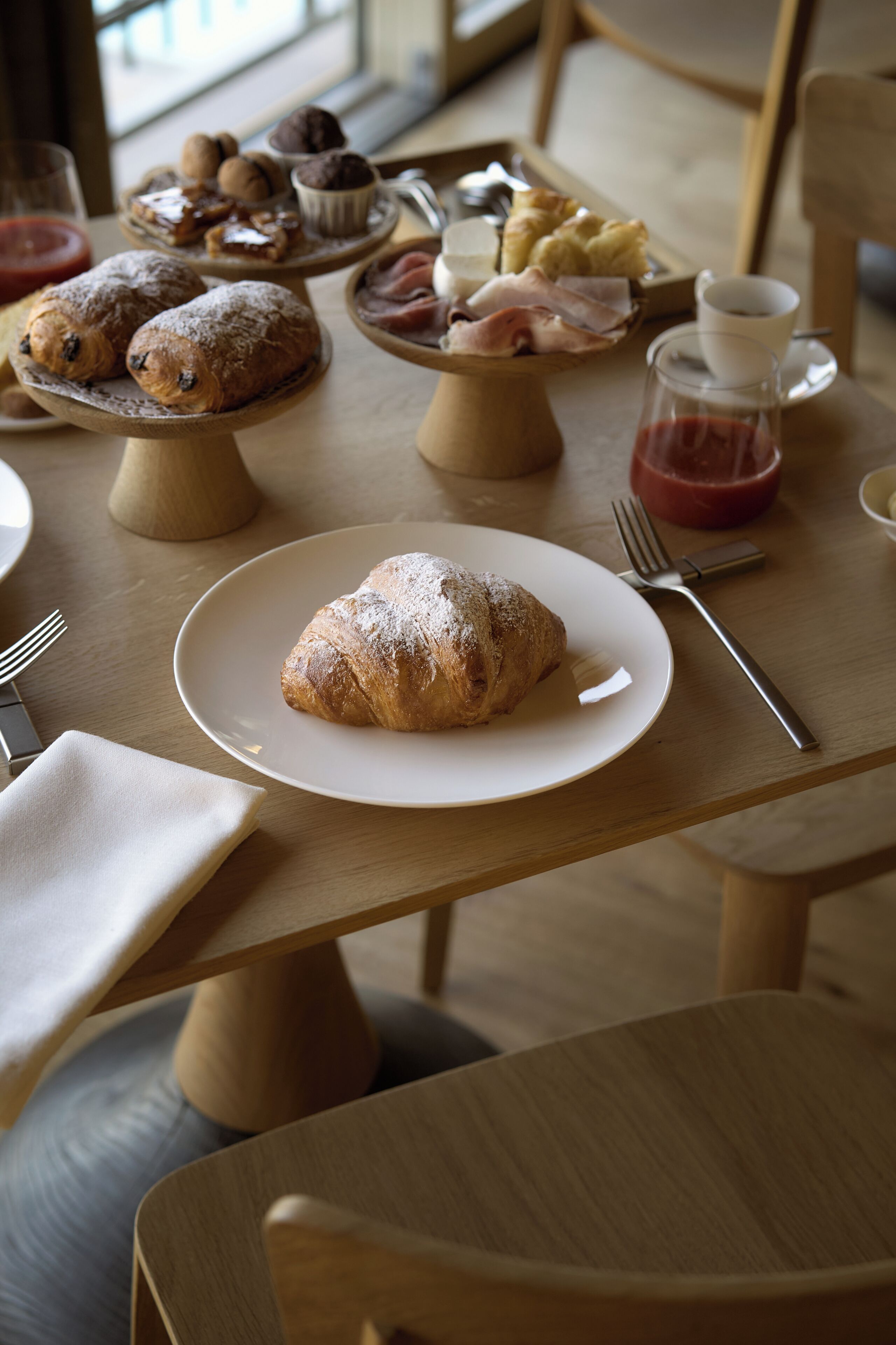 Een eettafel met een croissant, een kop koffie en verschillende gebakjes.