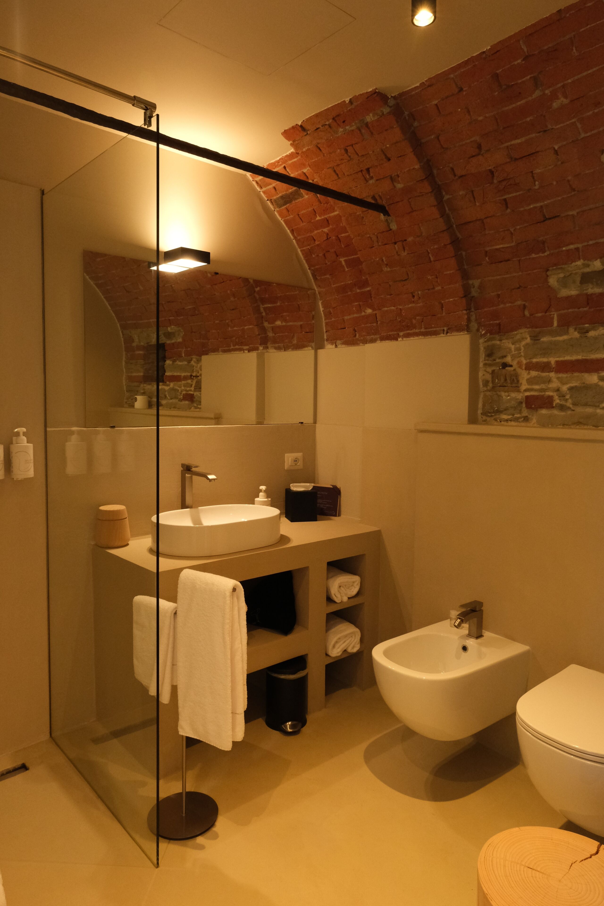 A modern bathroom with a glass-enclosed shower, a round sink, a bidet, and a mirror.