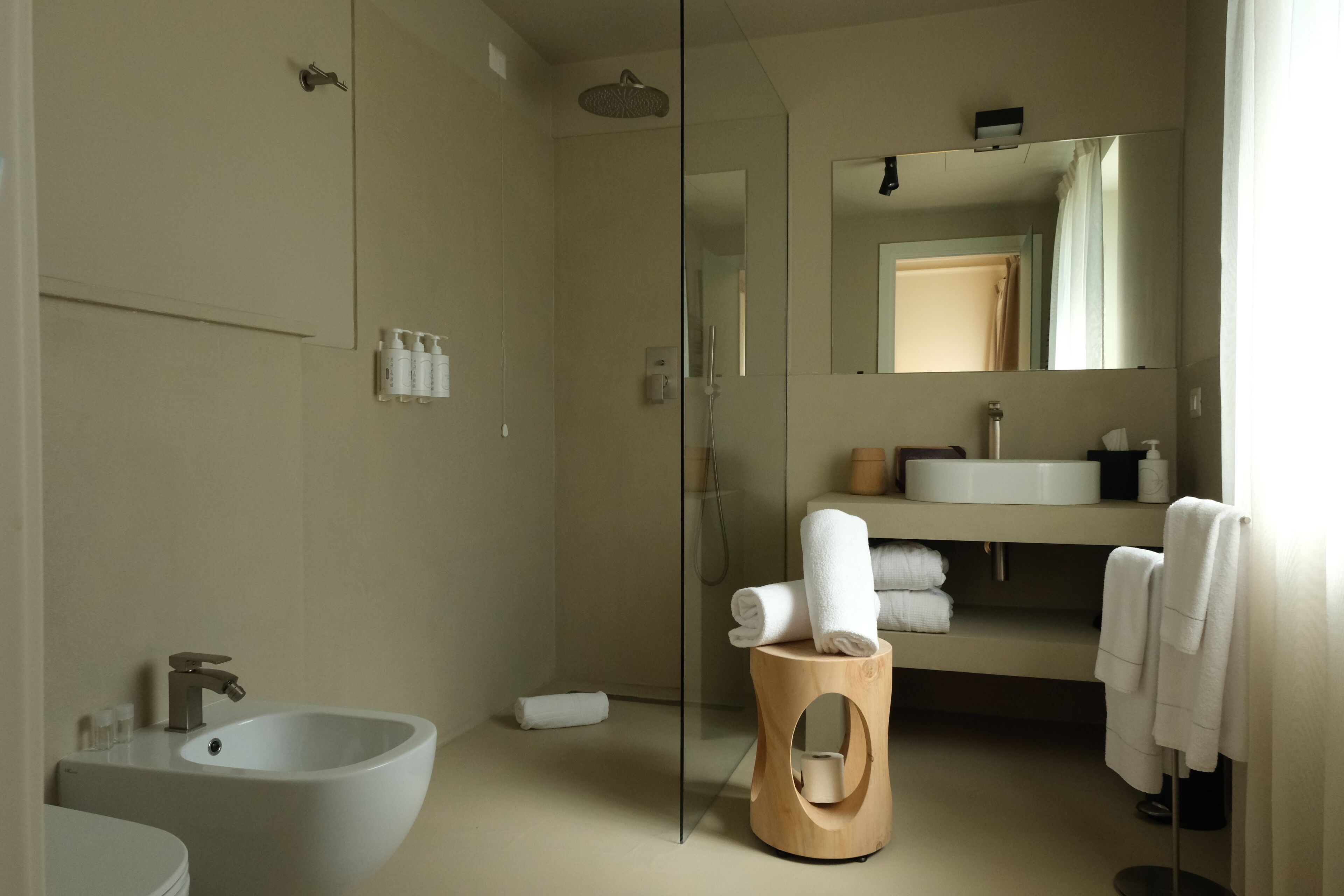 A modern bathroom with a glass-enclosed shower, a white sink, and a wooden stool.