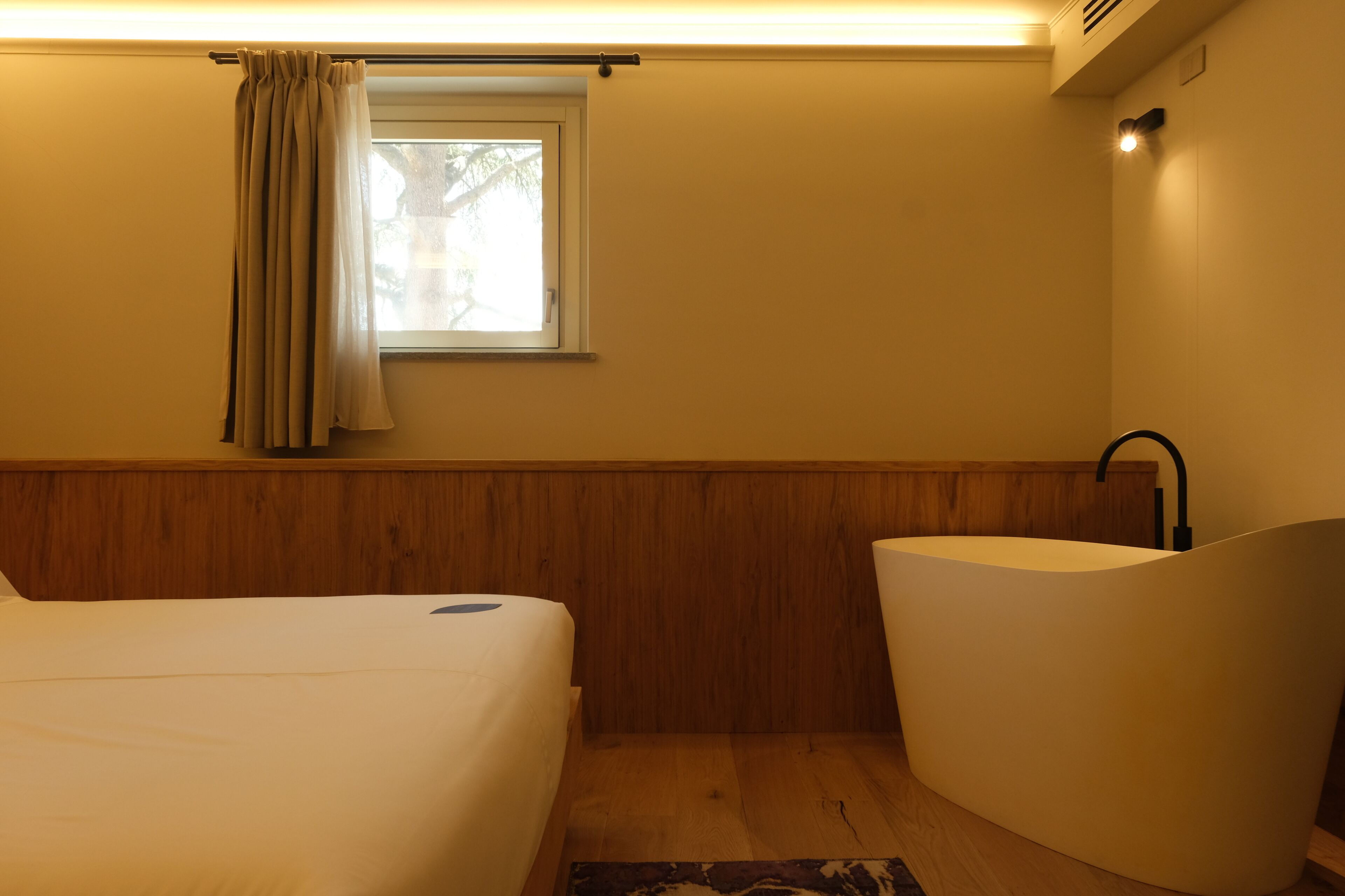A bedroom with a bed, a window with curtains, a sink, and a wooden floor.