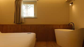 A bedroom with a bed, a window with curtains, a sink, and a wooden floor.