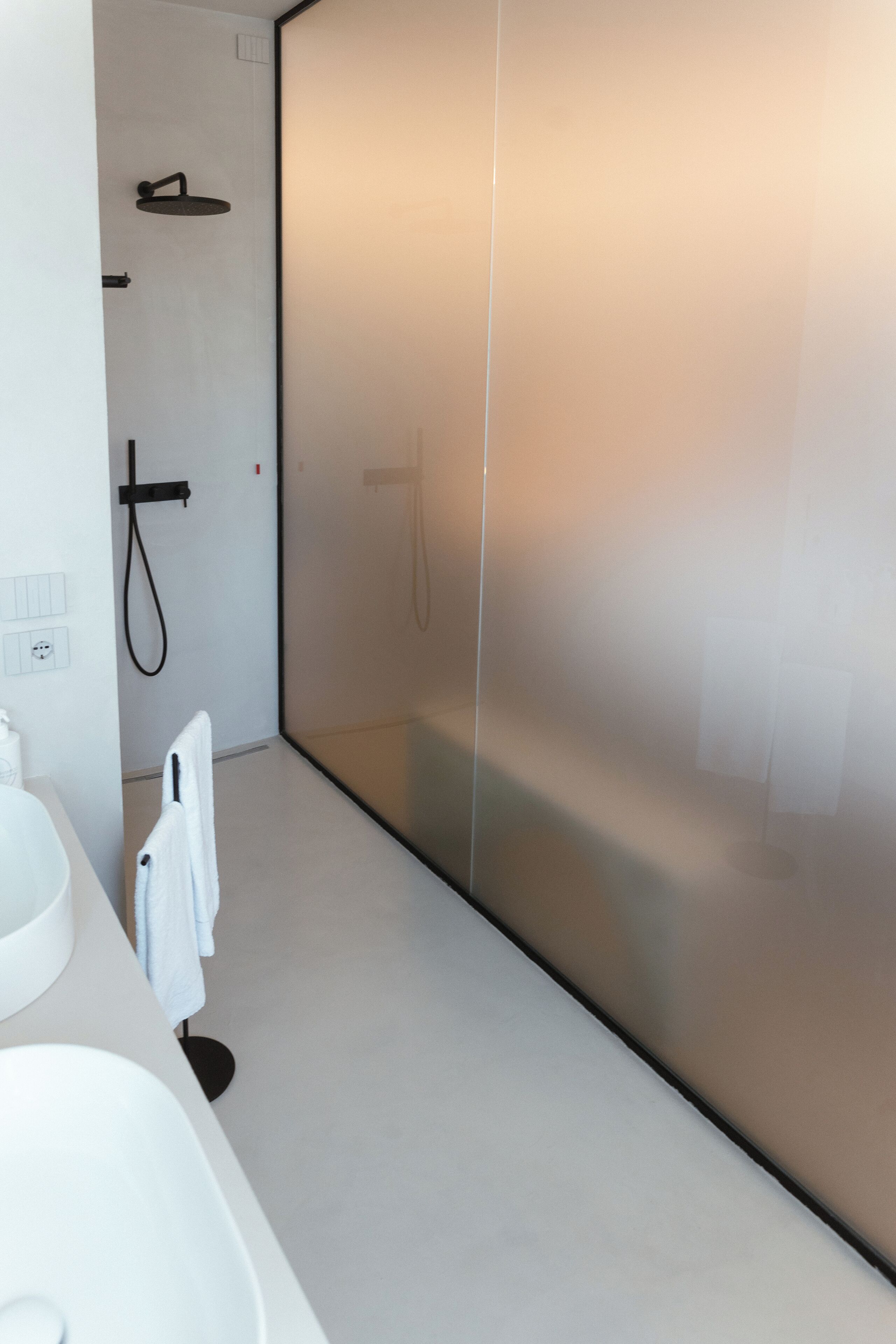 A modern bathroom with a white sink, a towel rack, and a glass shower enclosure.